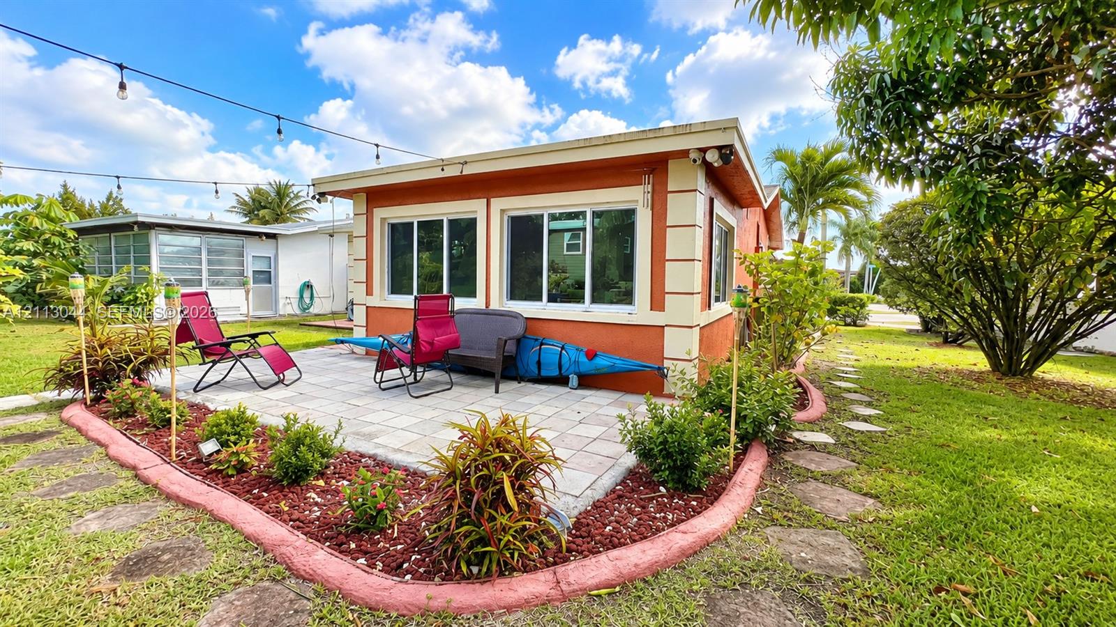 Exterior patio featuring paver flooring, landscaped garden beds with decorative borders, and string lighting