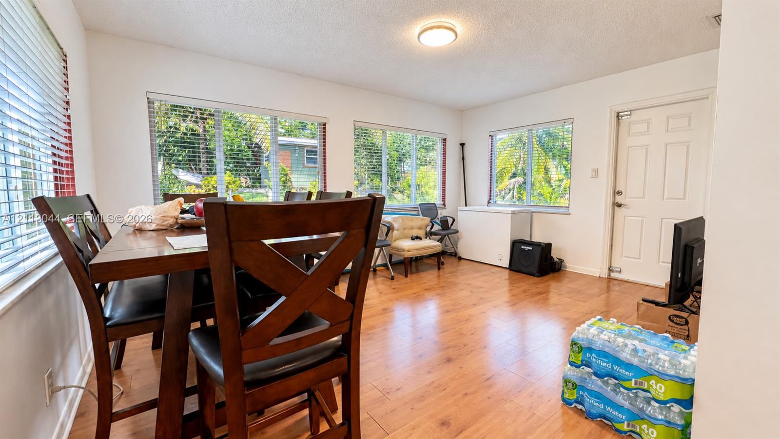 Spacious room featuring wood-finish flooring, large windows with horizontal blinds, and a solid-core entry door