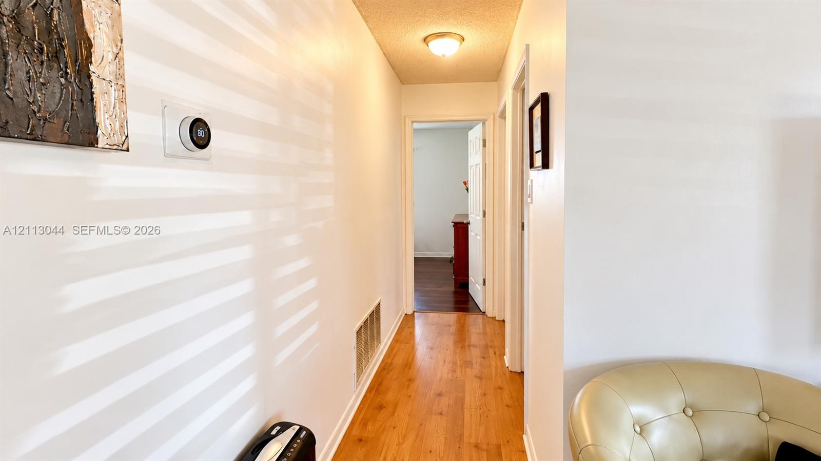 Hallway featuring wood-finish flooring, white walls, flush-mount ceiling lighting, and a smart thermostat