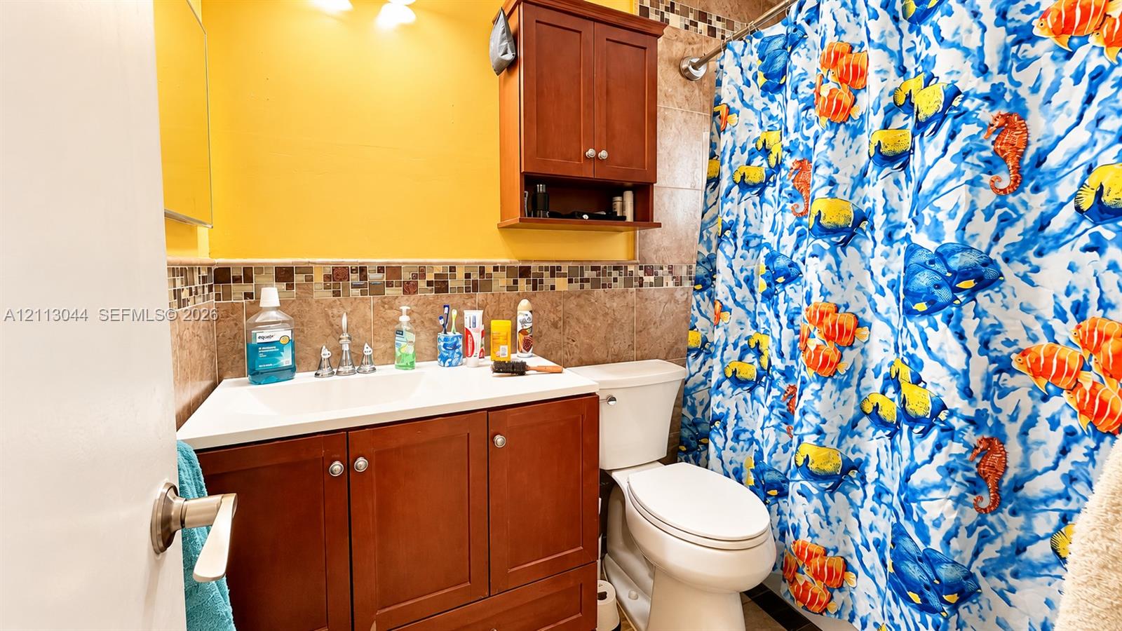 Bathroom featuring a wood-finish vanity with a white integrated sink, ceramic wall tiling with a mosaic glass accent border, and a built-in wood-finish wall cabinet