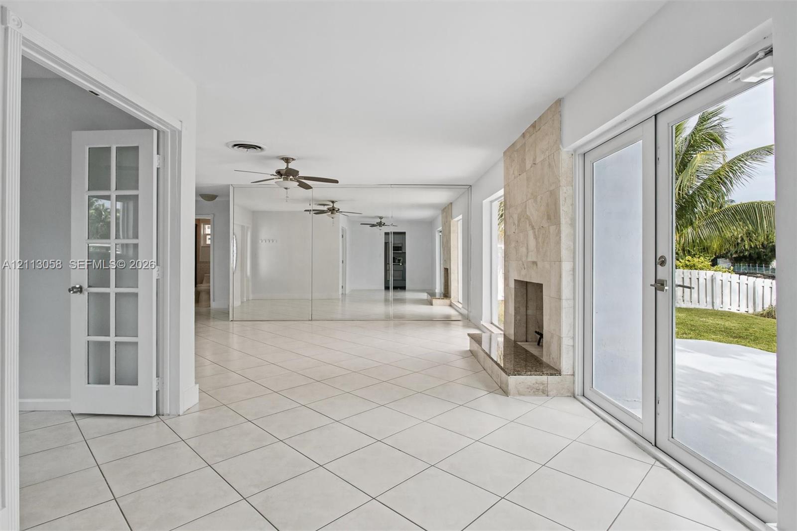 Tile flooring, floor-to-ceiling mirrored walls, stone-surround fireplace with a hearth, and glass-paned French doors