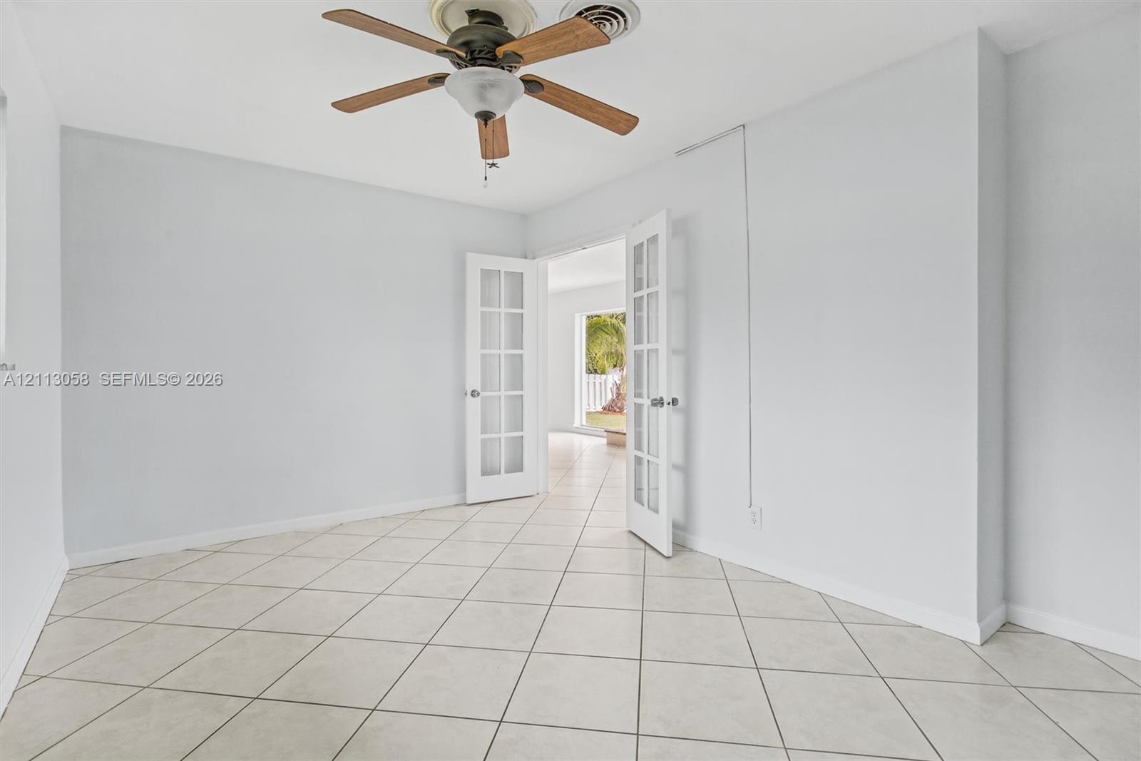 Interior space featuring large-format diagonal tile flooring, white French doors with glass panes, and a ceiling-mounted fan with wood-finish blades