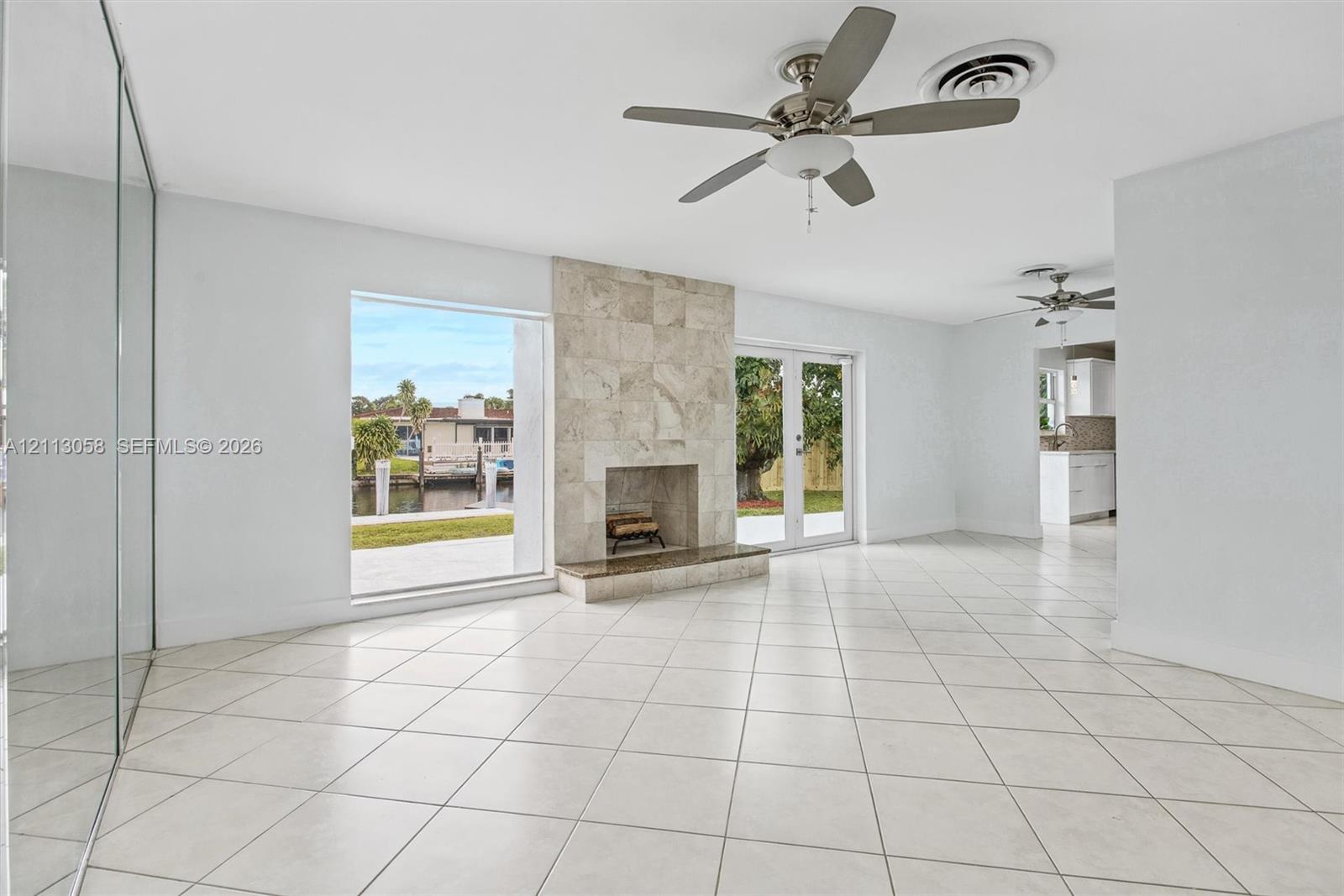Living area featuring tile flooring, a floor-to-ceiling stone-tiled fireplace, dual ceiling fans, a large picture window, and glass-paned double doors