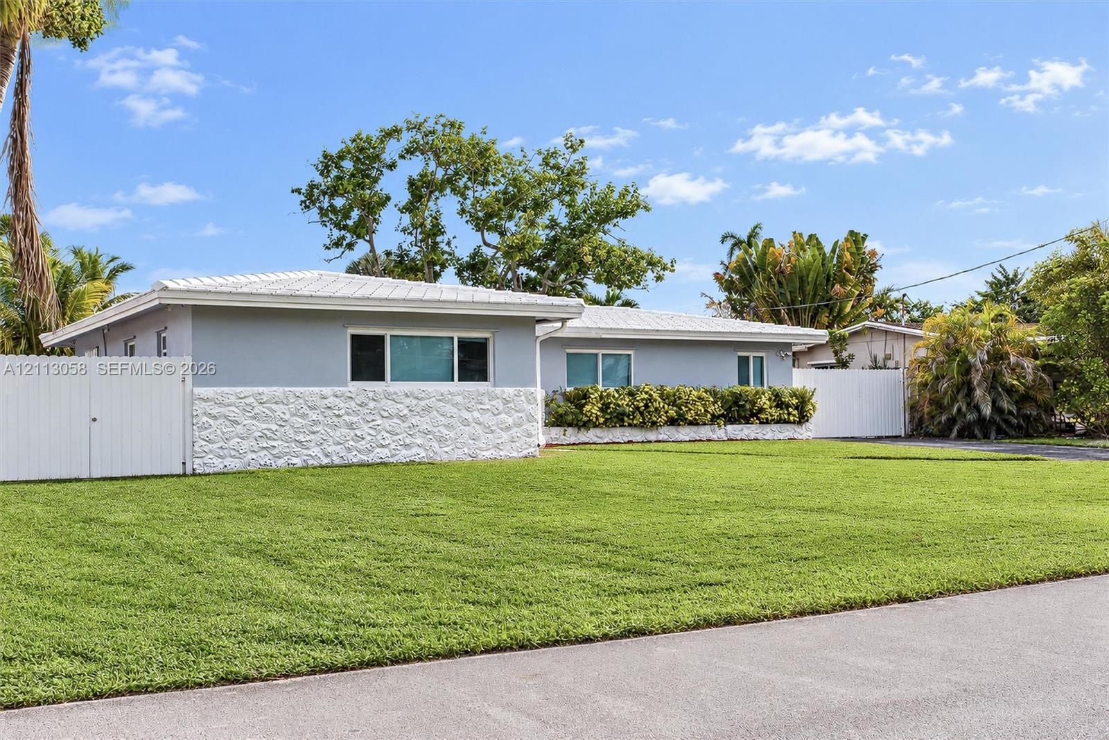 Single-story residence featuring a textured masonry facade, light-toned exterior finish, metal roofing, and privacy fencing enclosing the perimeter