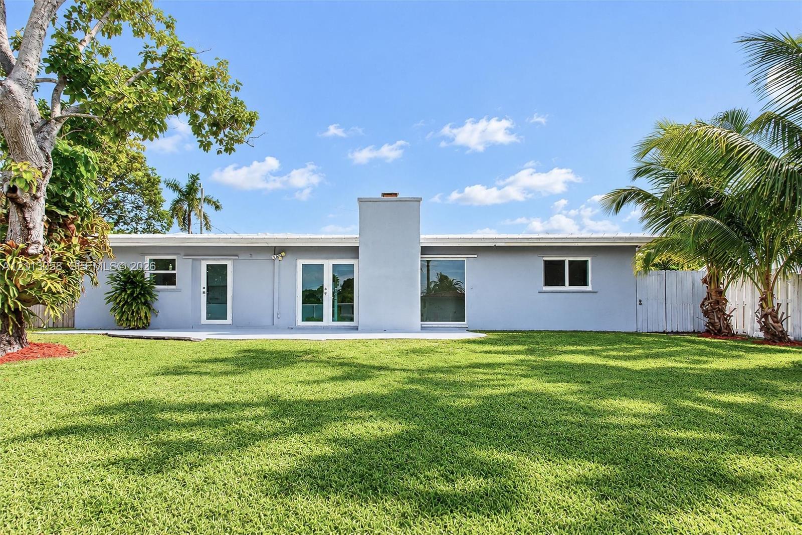 Single-story exterior featuring a concrete patio, exterior masonry chimney, dual glass panel entry doors, and mature landscaping