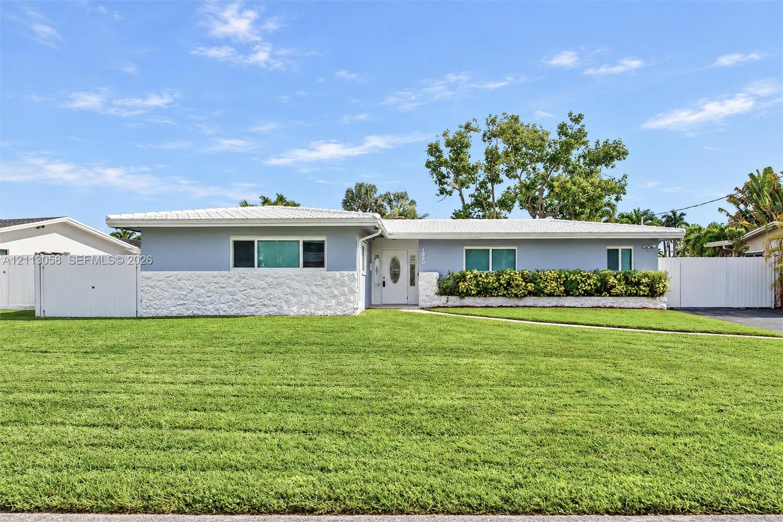 Single-story exterior featuring light-toned masonry, textured stone wainscoting, a covered entry with an oval-glass door, and vinyl perimeter fencing