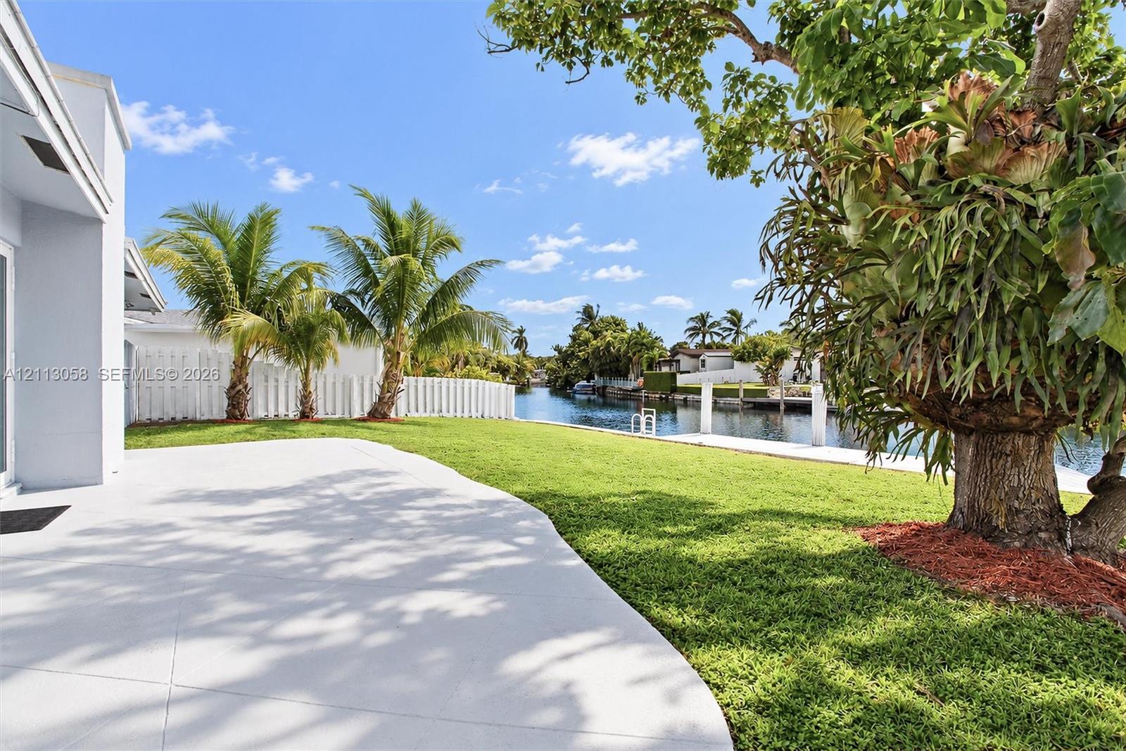 Waterfront backyard featuring a concrete patio, a manicured lawn, palm trees, and a private dock