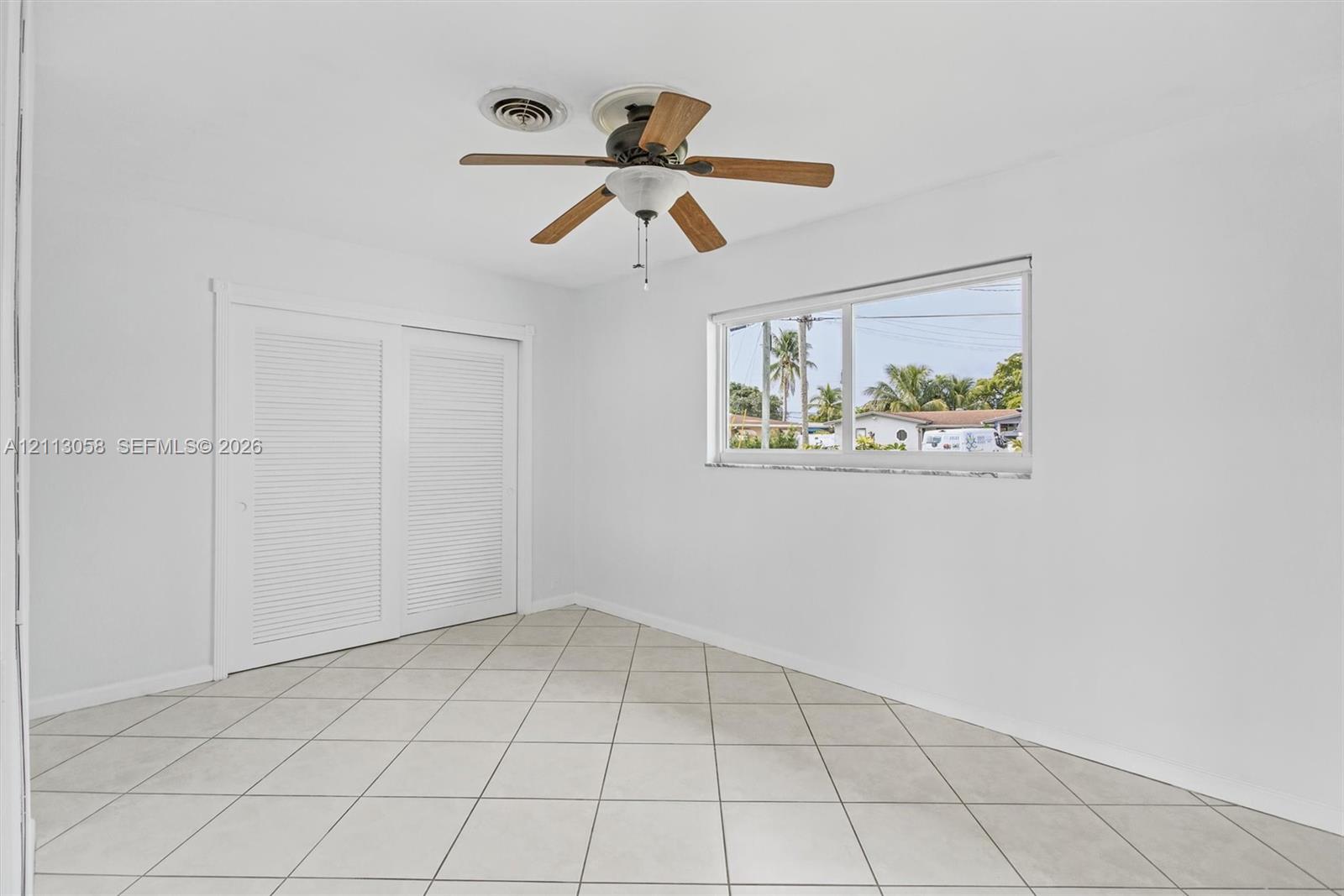 Interior space featuring neutral tile flooring, louvered closet doors, and a ceiling fan with integrated lighting