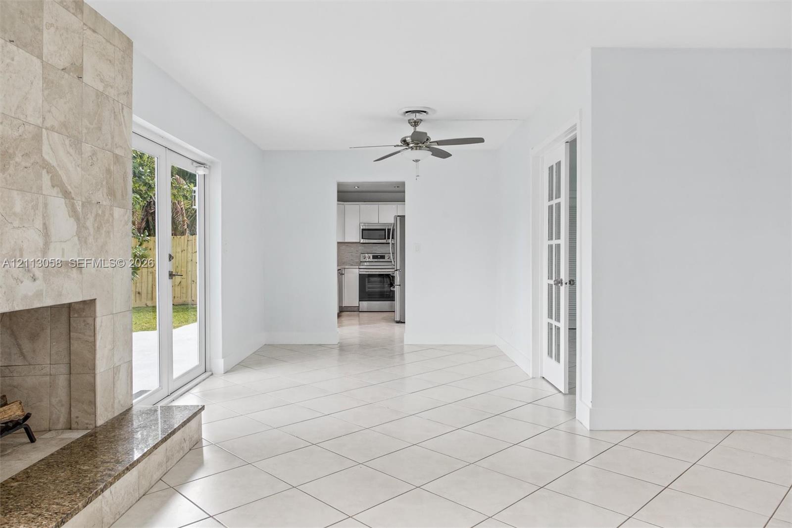 Stone-clad fireplace with a polished hearth, ceramic tile flooring set on a diagonal, French doors with glass panes, and a ceiling fan