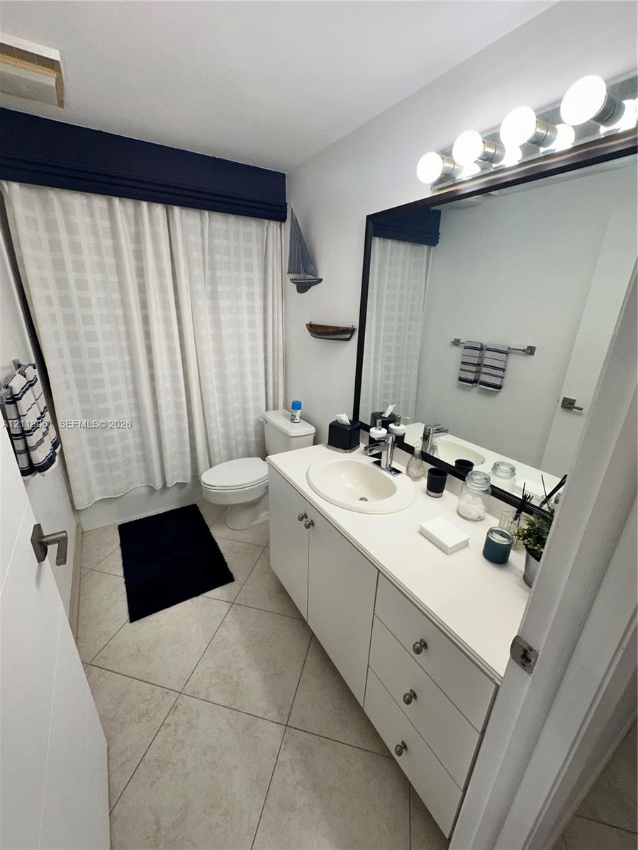 Bathroom featuring a vanity with a white countertop and oval undermount sink, large wall-mounted mirror, multi-bulb light fixture, and stone-finish floor tile
