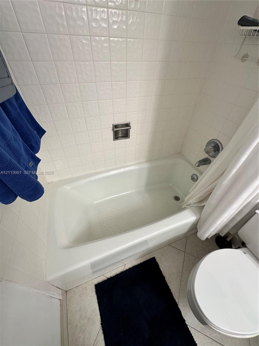Full-size soaking tub featuring a metallic faucet, integrated shower diverter, inset metal recessed niche, and white tiled surround