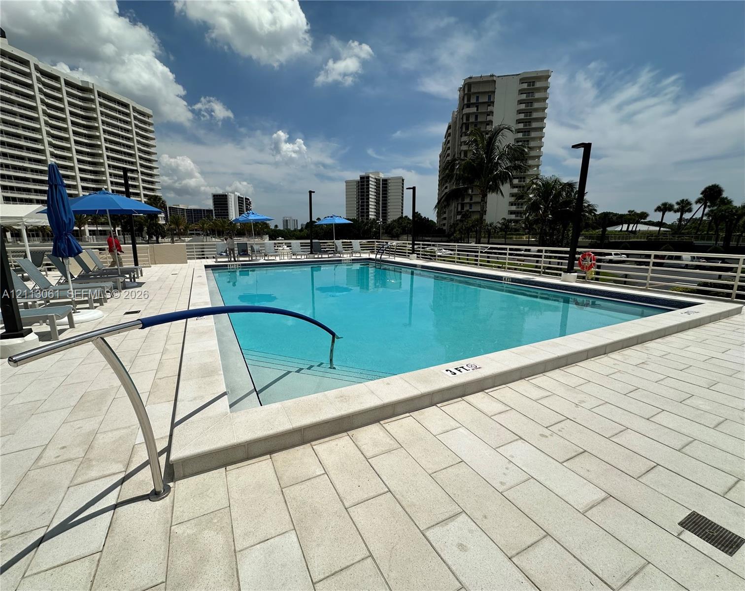 Rectangular swimming pool featuring a light-toned stone deck, built-in entry steps, and a metal safety handrail