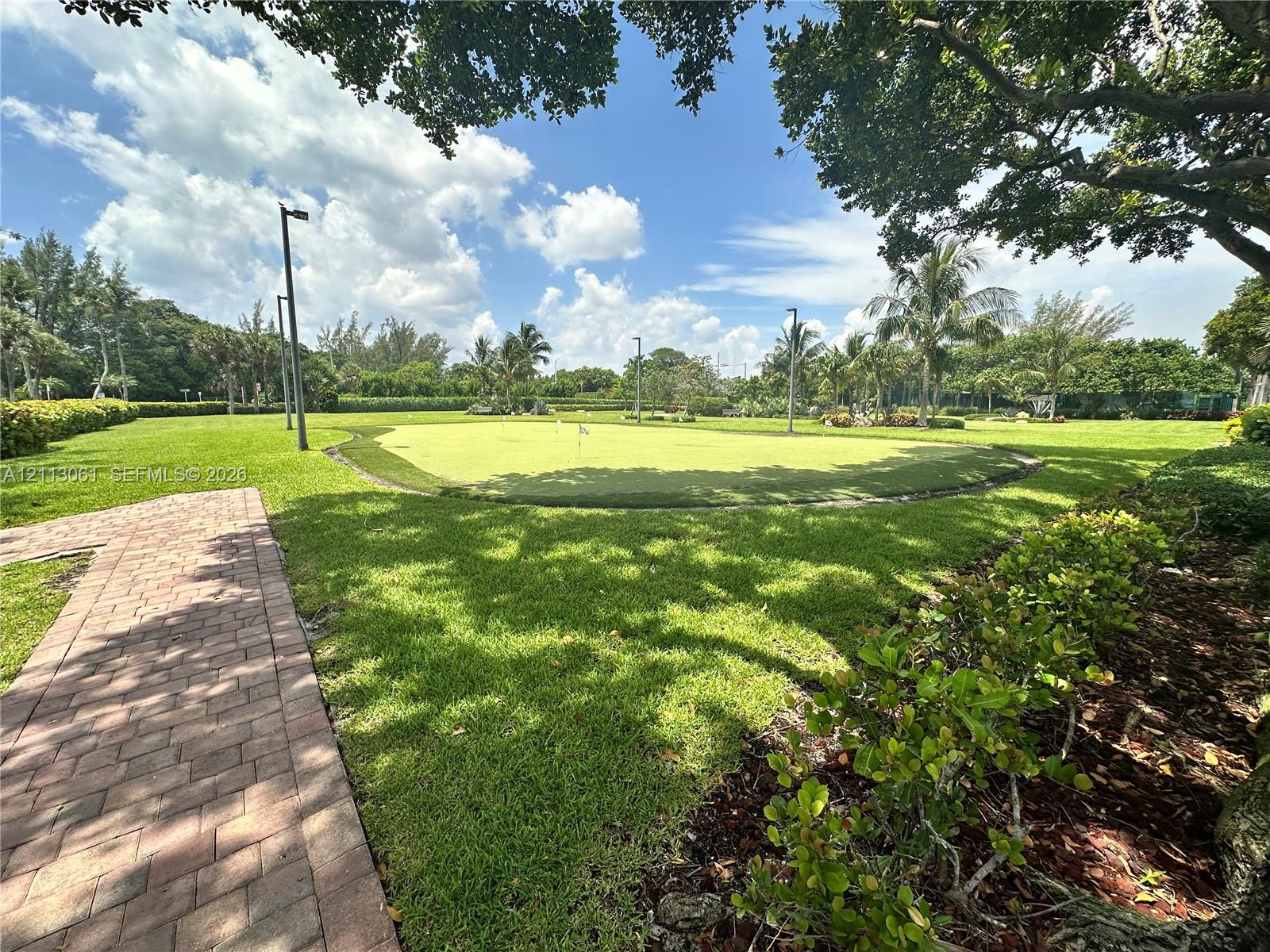 Expansive grounds featuring a private putting green, paver walkway, manicured lawn, and mature canopy trees