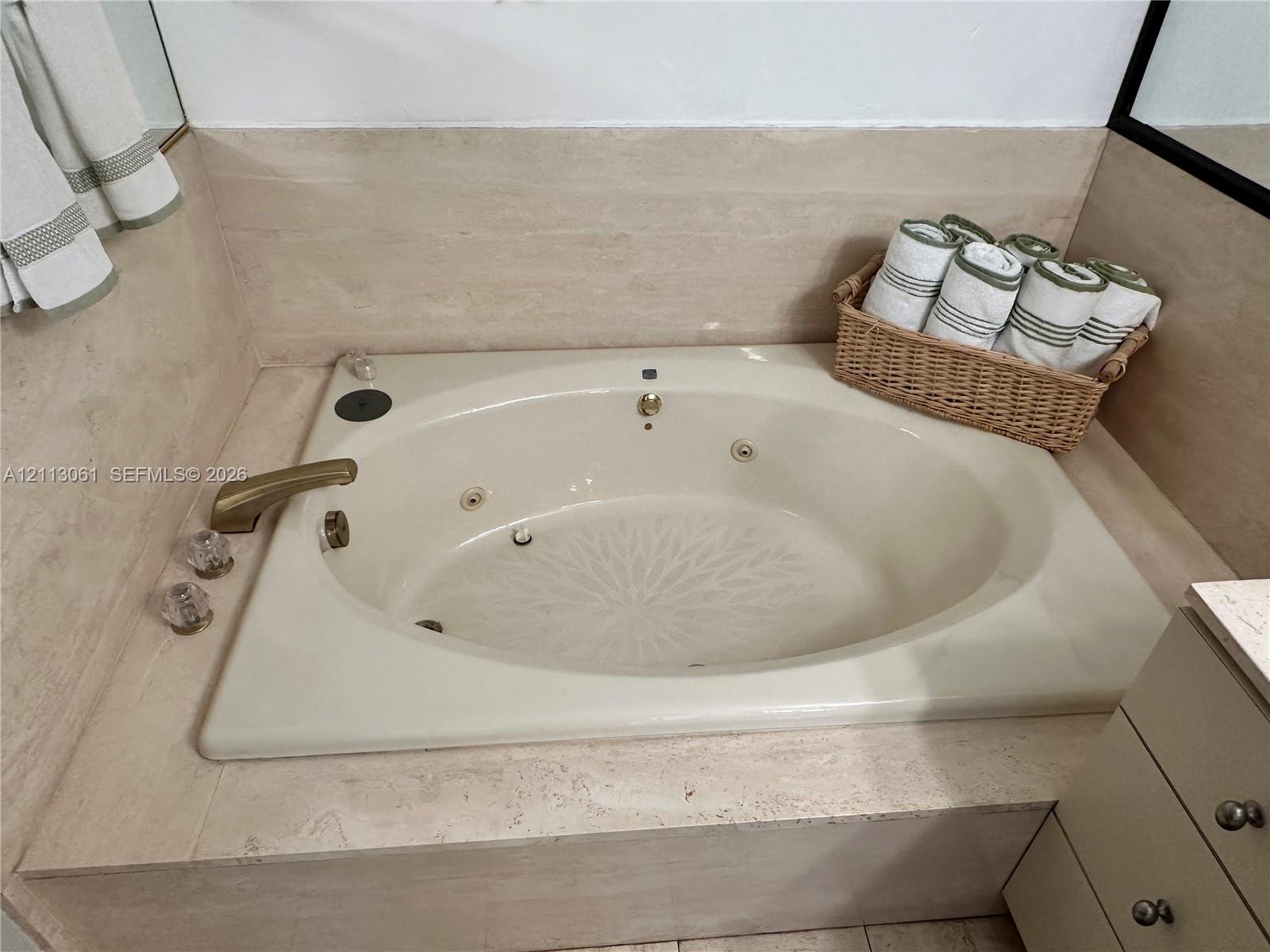 Drop-in soaking tub with integrated water jets, stone-tiled surround, and metallic finish faucet hardware