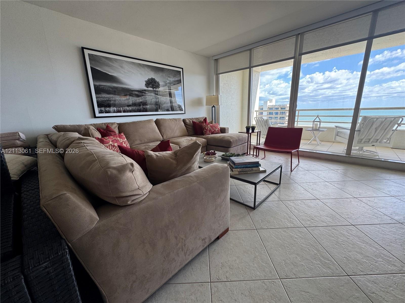 Floor-to-ceiling glass sliding doors, ceramic tile flooring, and a private balcony with water scenery