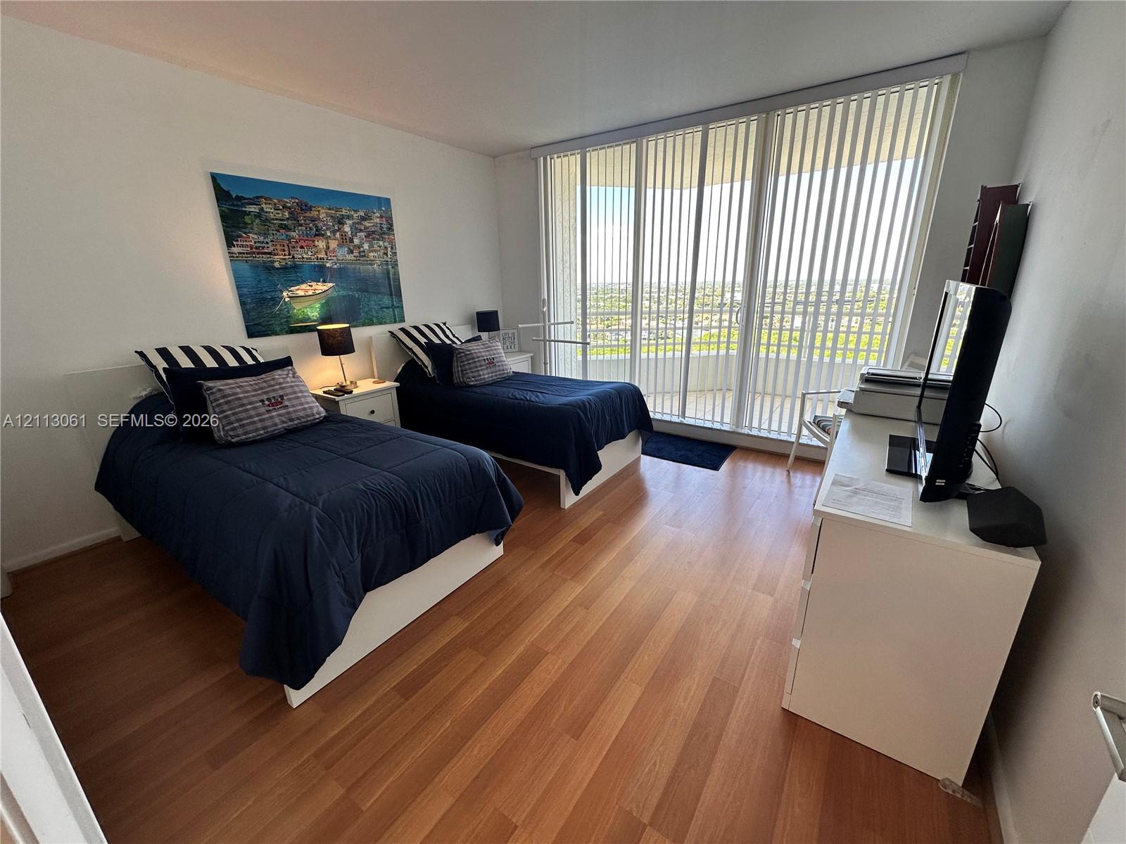 Room featuring wood-finish flooring, floor-to-ceiling glass wall, vertical window blinds, and balcony access