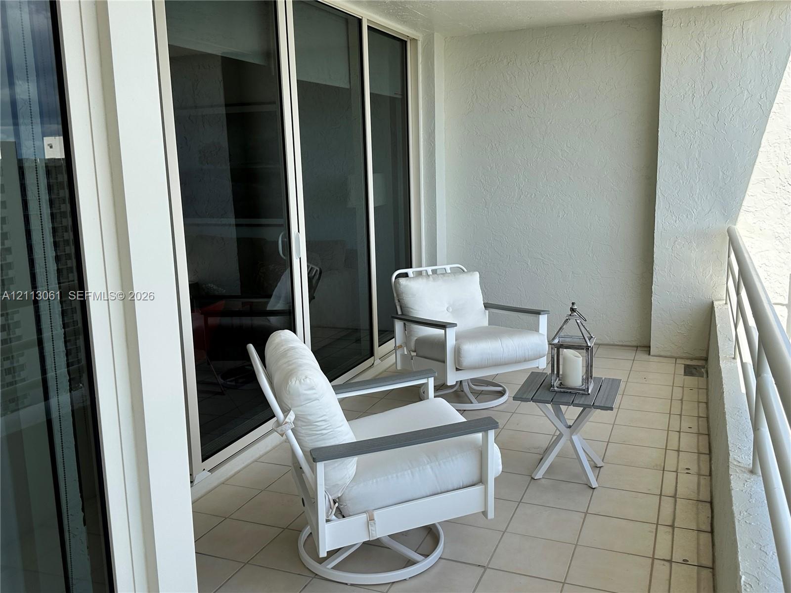 Covered balcony featuring neutral ceramic tile flooring, textured stucco walls, and floor-to-ceiling sliding glass doors with aluminum framing