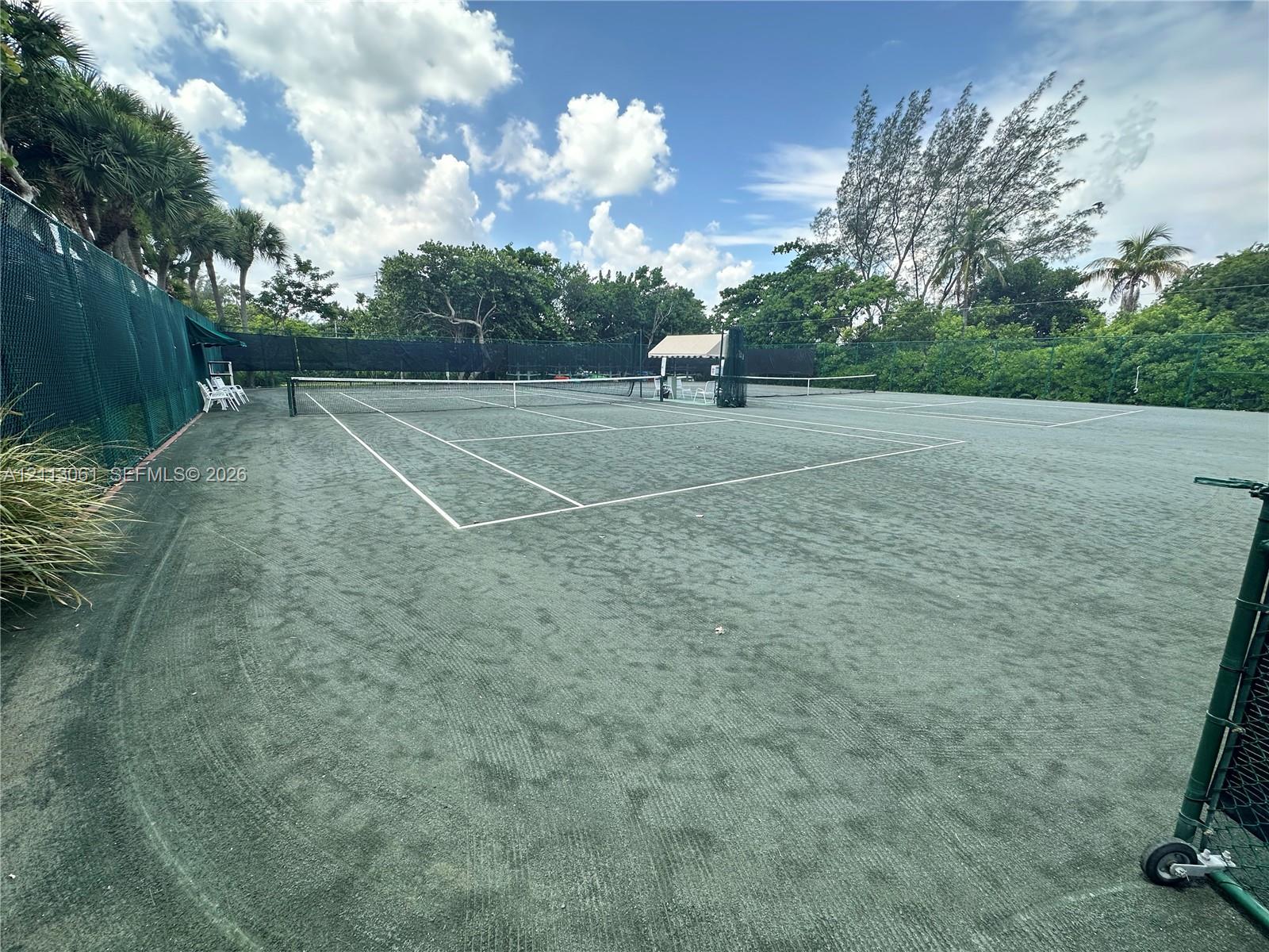 Tennis court with green synthetic surface, perimeter mesh fencing, and net system