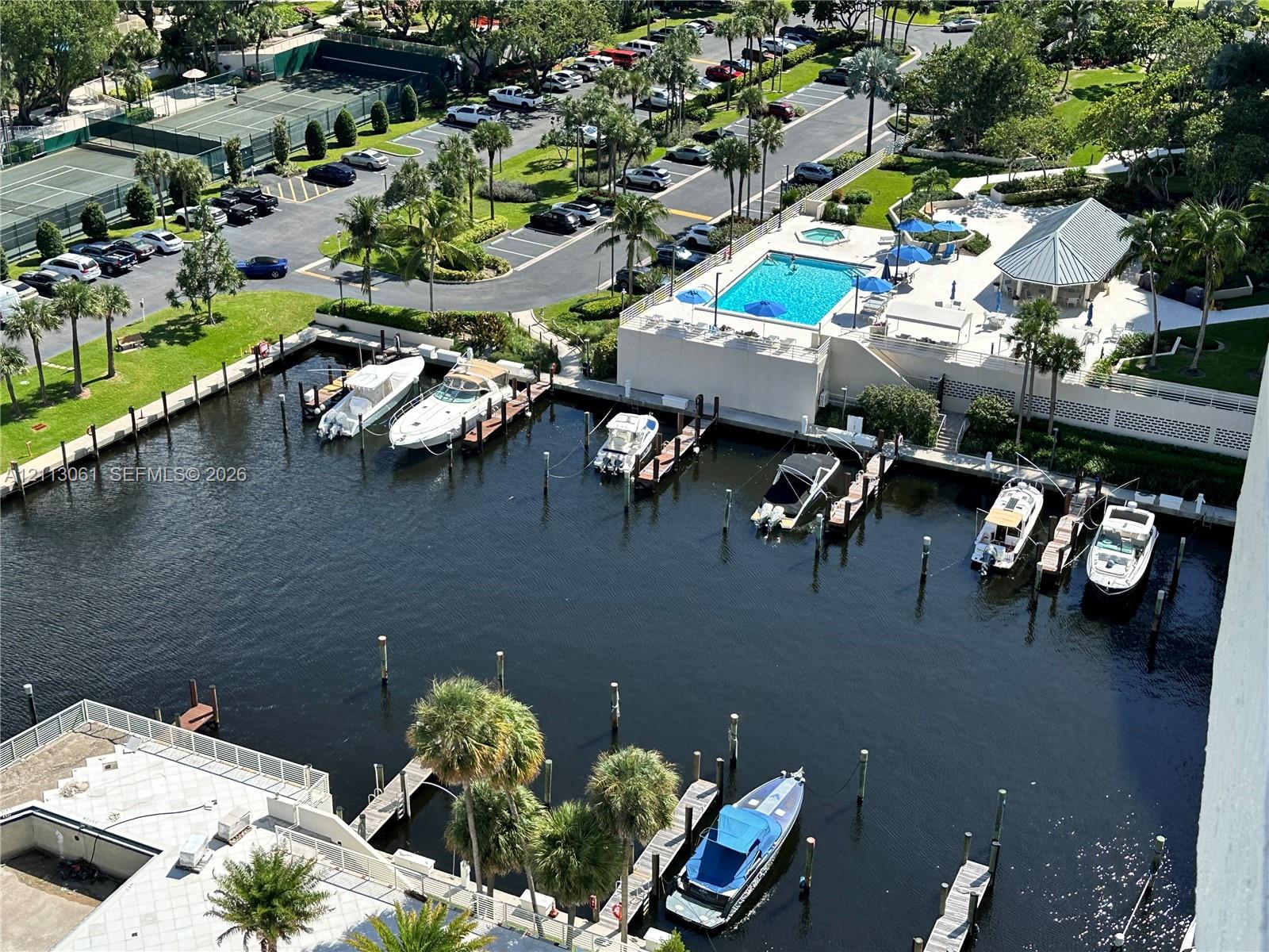 Aerial perspective of the deep-water marina featuring multiple boat slips, a swimming pool, a covered pavilion, and hard-court tennis facilities