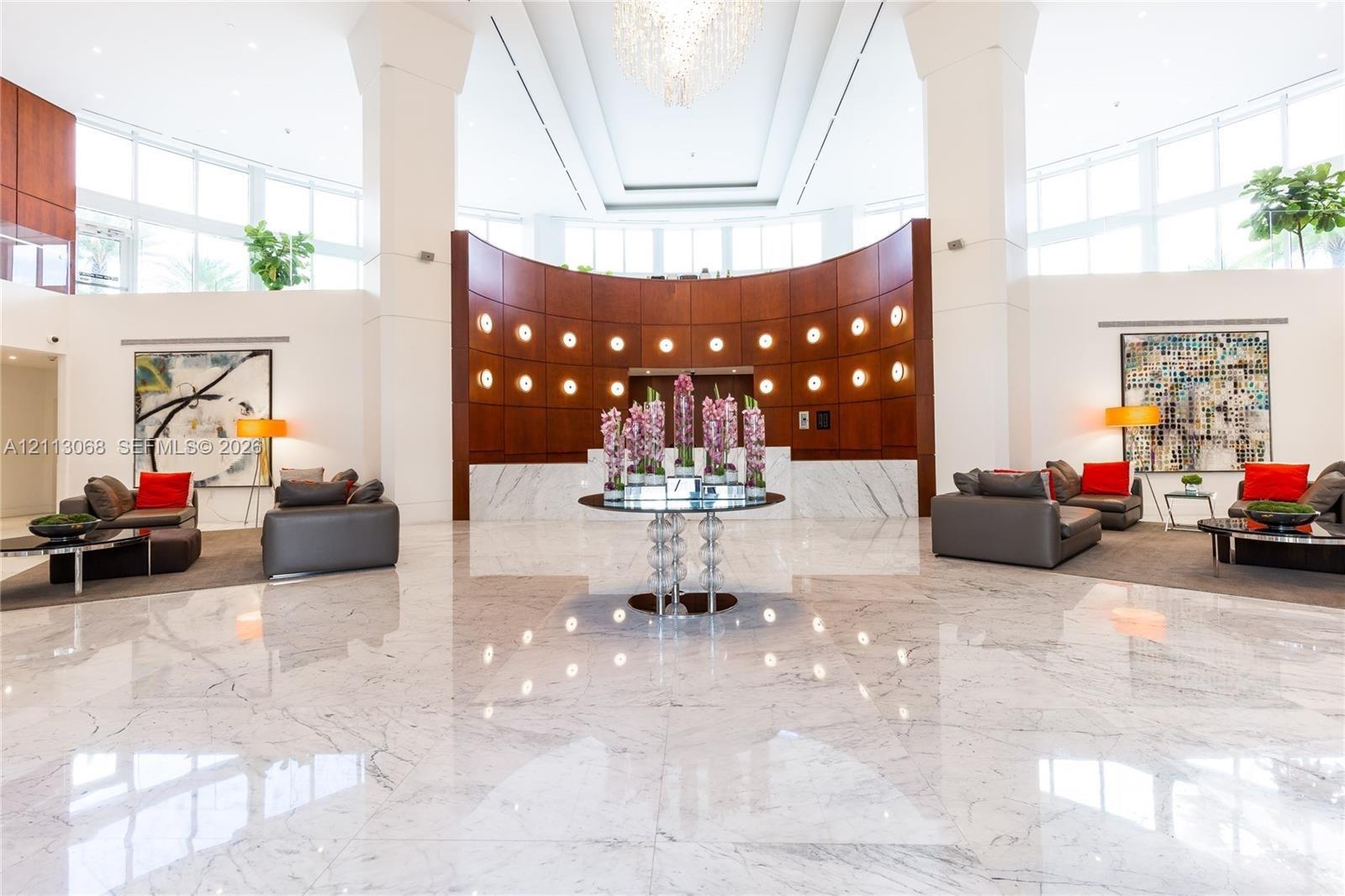 Grand lobby featuring polished stone flooring, vaulted ceilings, curved wood-paneled wall, recessed circular lighting, and large-scale windows