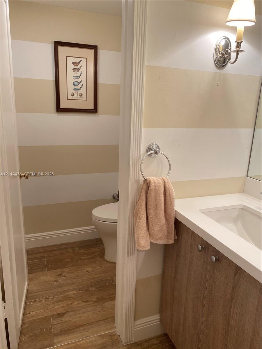 Bathroom featuring wood-finish flooring, a vanity with a white countertop and integrated sink, a wall-mounted light fixture, and a circular towel ring