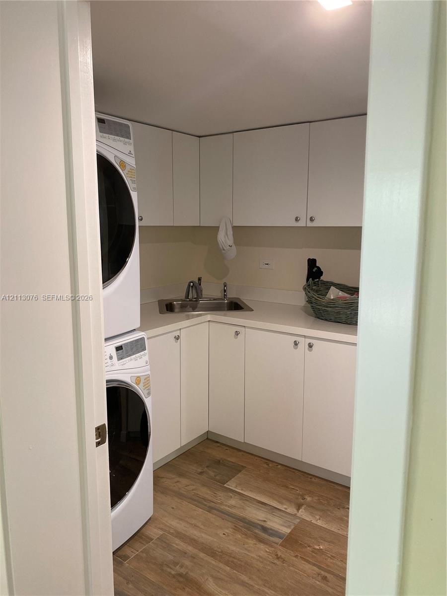 Laundry area featuring white cabinetry, solid-surface countertop, stainless steel sink with faucet, and wood-finish flooring