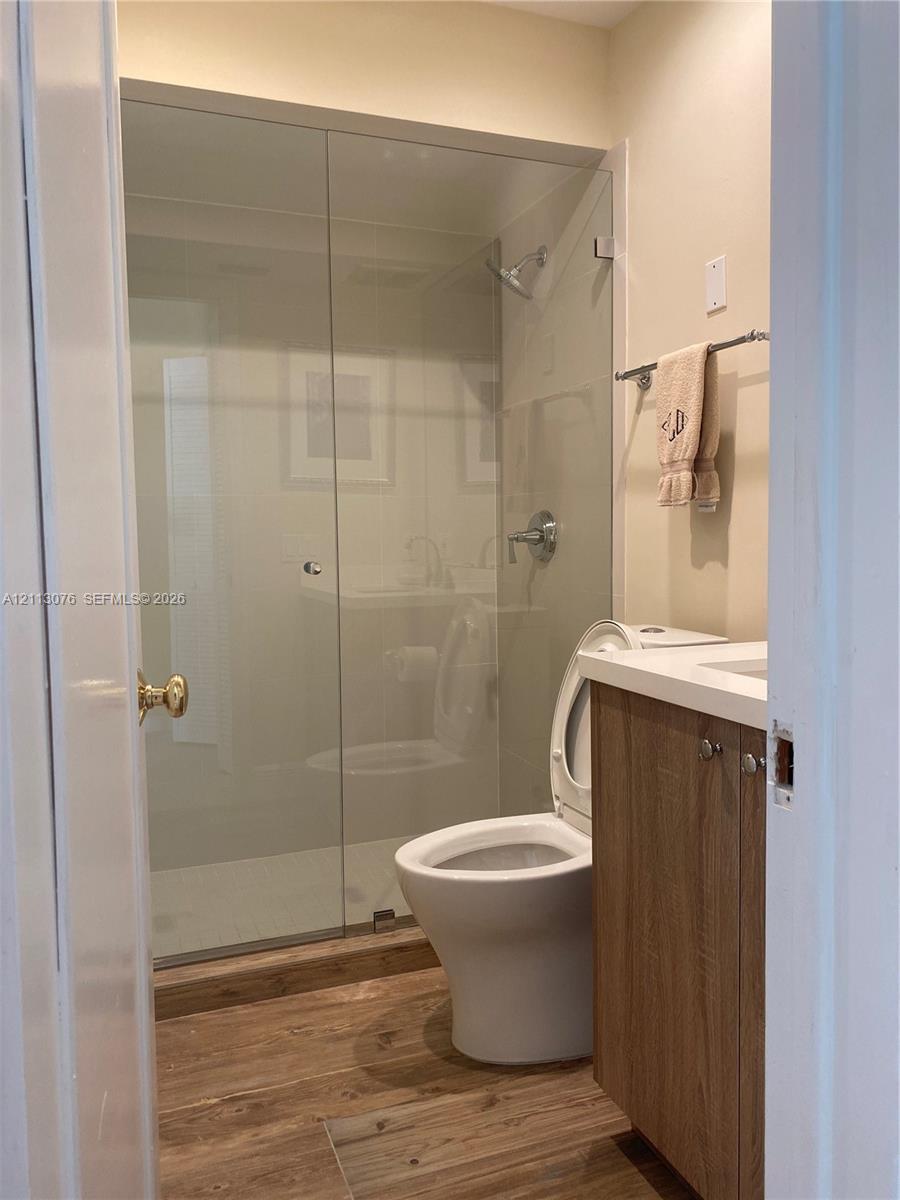 Bathroom featuring wood-finish flooring, a frameless glass shower enclosure, a vanity with a light-toned countertop, and chrome hardware
