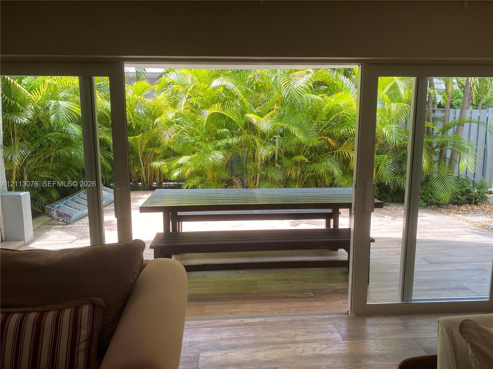 Exterior patio featuring light-toned tile flooring, framed by mature perimeter palm trees and horizontal privacy fencing
