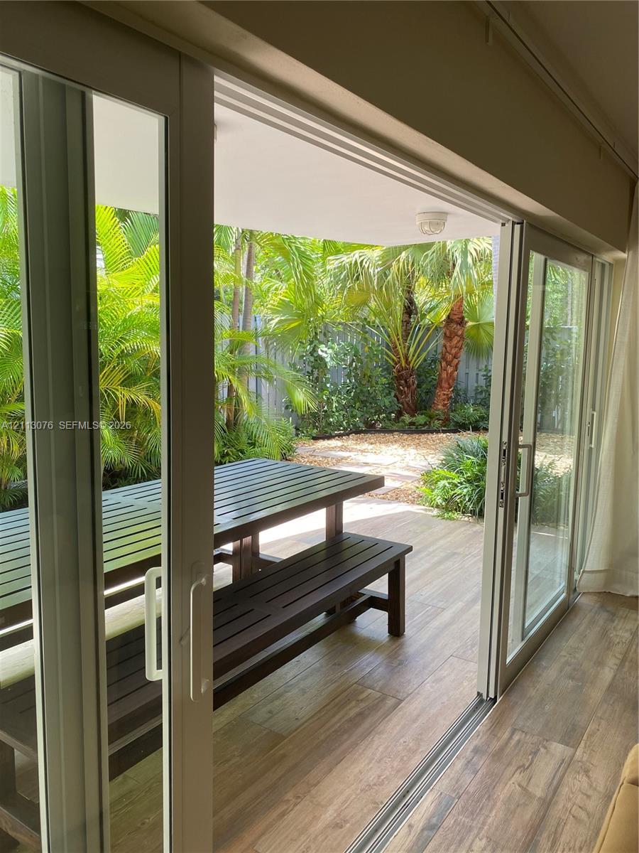 Sliding glass doors featuring white frames, wood-finish flooring, covered patio space, and landscape elements including palm trees