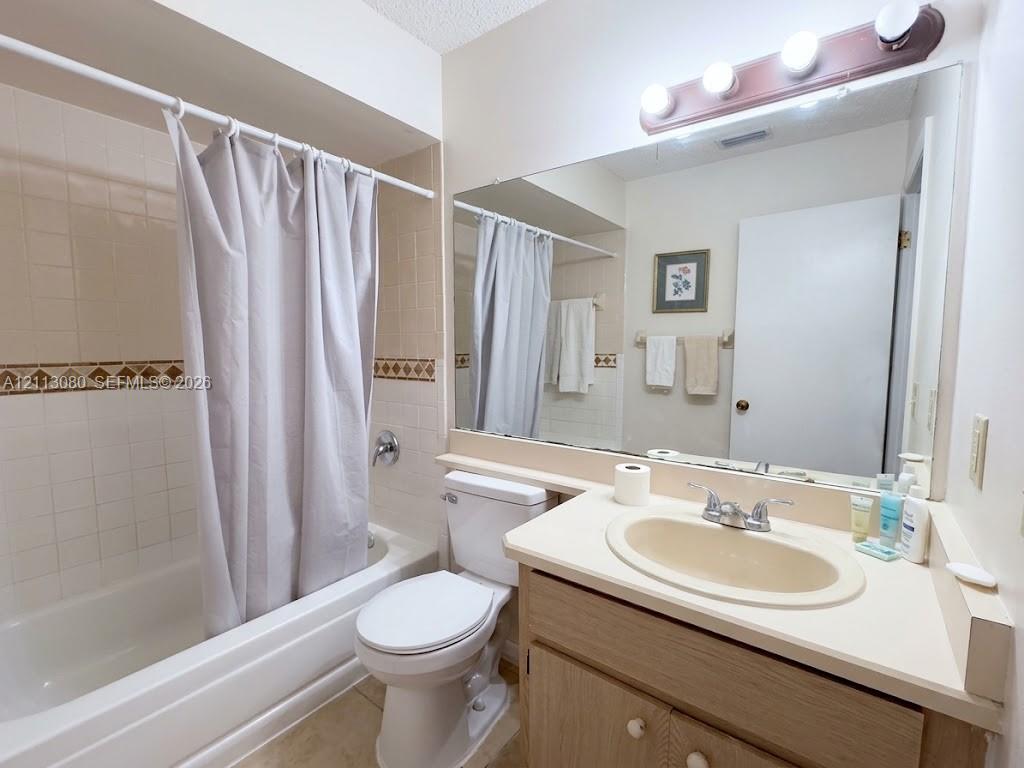 Full-width wall mirror, vanity cabinet with integrated sink, porcelain-finish bathtub with tiled surround, and decorative accent tile border
