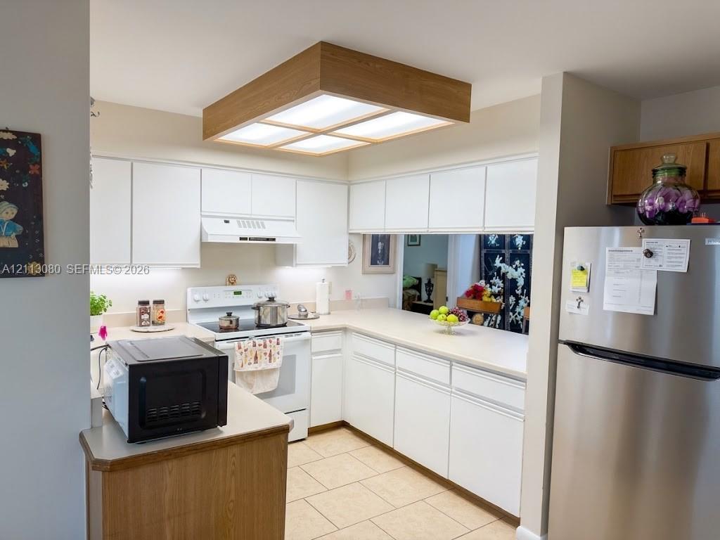 Kitchen featuring white cabinetry, light-toned countertops, tile flooring, stainless steel refrigerator, and wood-trimmed recessed lighting