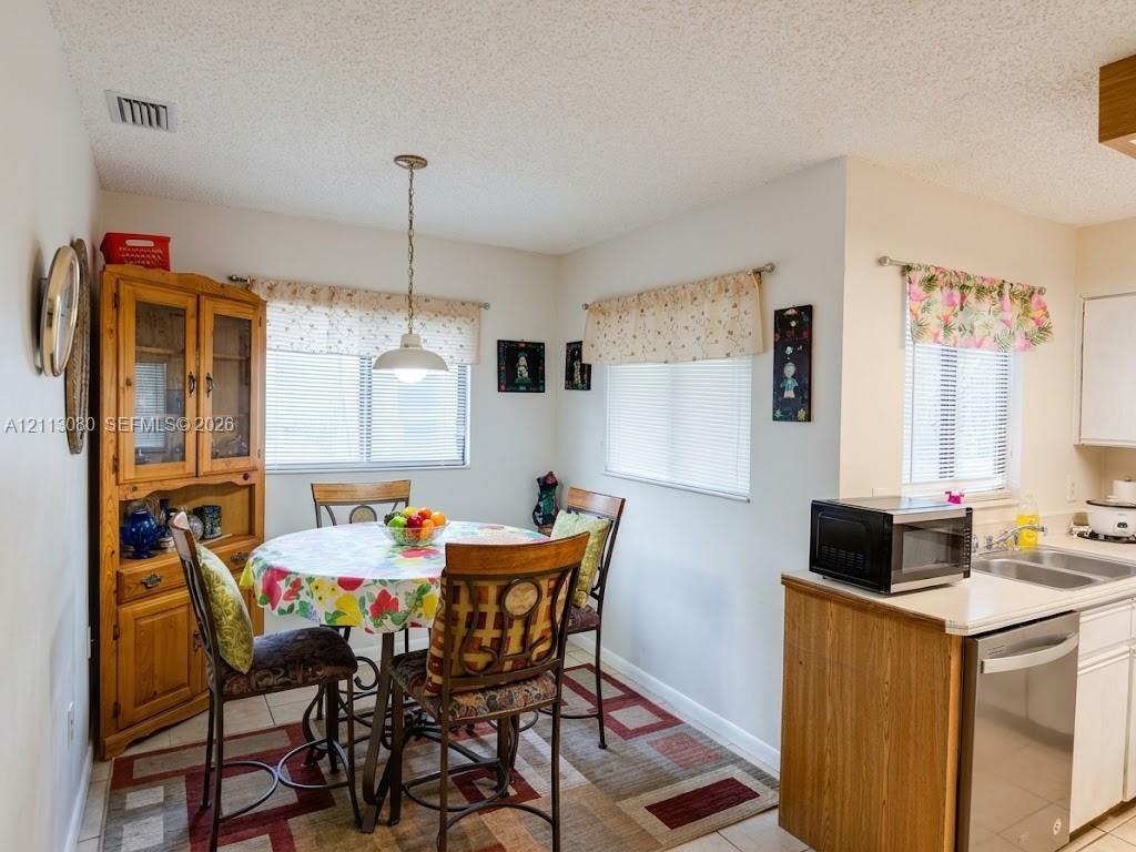 Kitchen area featuring tile flooring, three large windows with neutral valances, a stainless steel dishwasher, and a built-in wooden cabinet