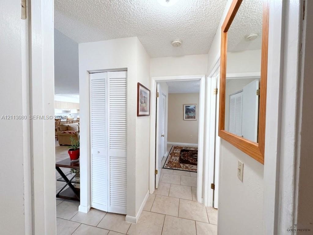 Interior hallway featuring neutral ceramic tile flooring, a built-in white bifold closet door, and a wall-mounted wooden-framed mirror