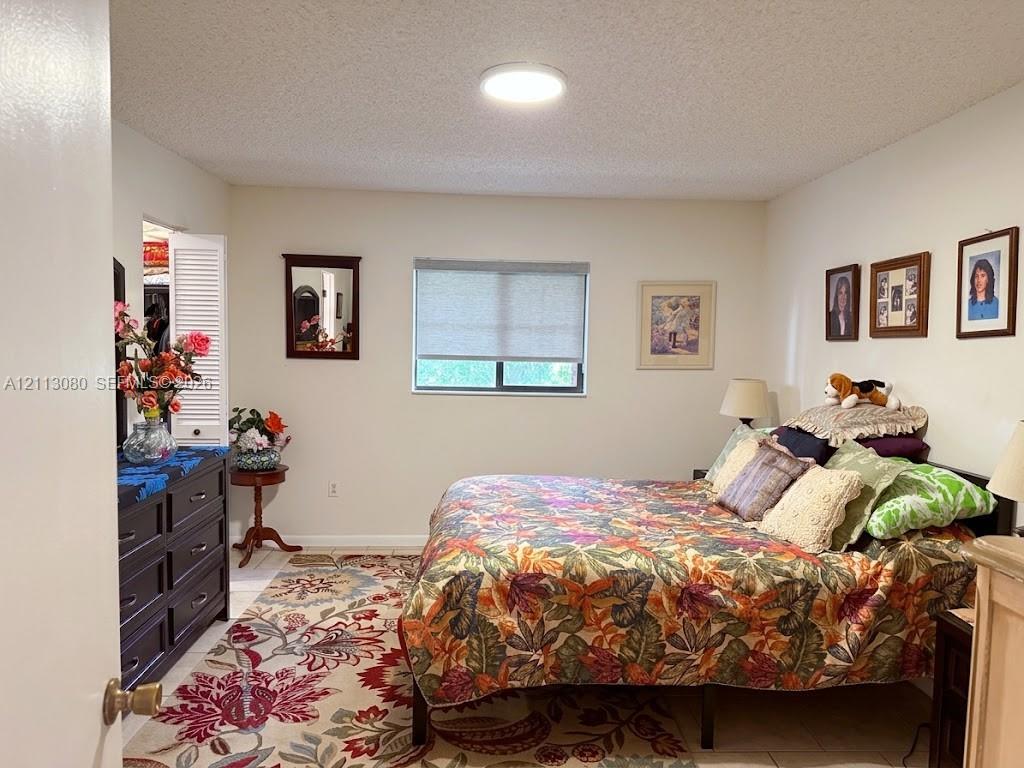 Neutral-toned room featuring a single-hung window with a roller shade, light-colored tile flooring, flush-mount ceiling lighting, and a closet with louvered double doors