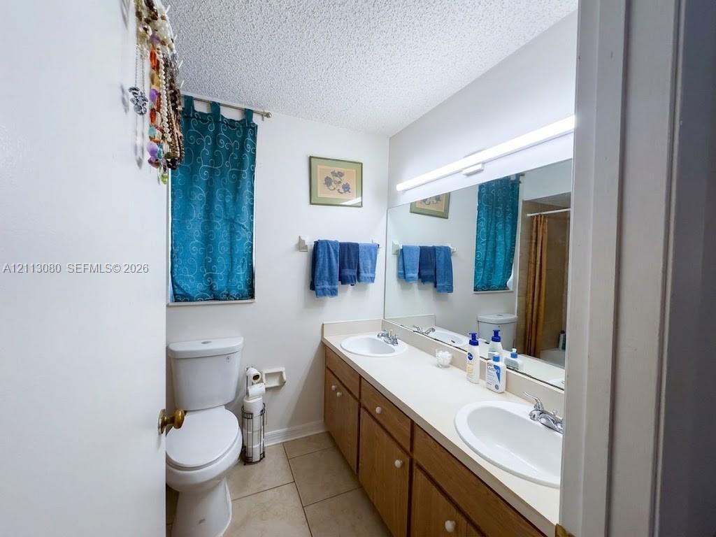 Bathroom featuring a double vanity with integrated oval sinks, solid surface countertop, wood-finish cabinetry, and large wall-mounted mirror with integrated lighting