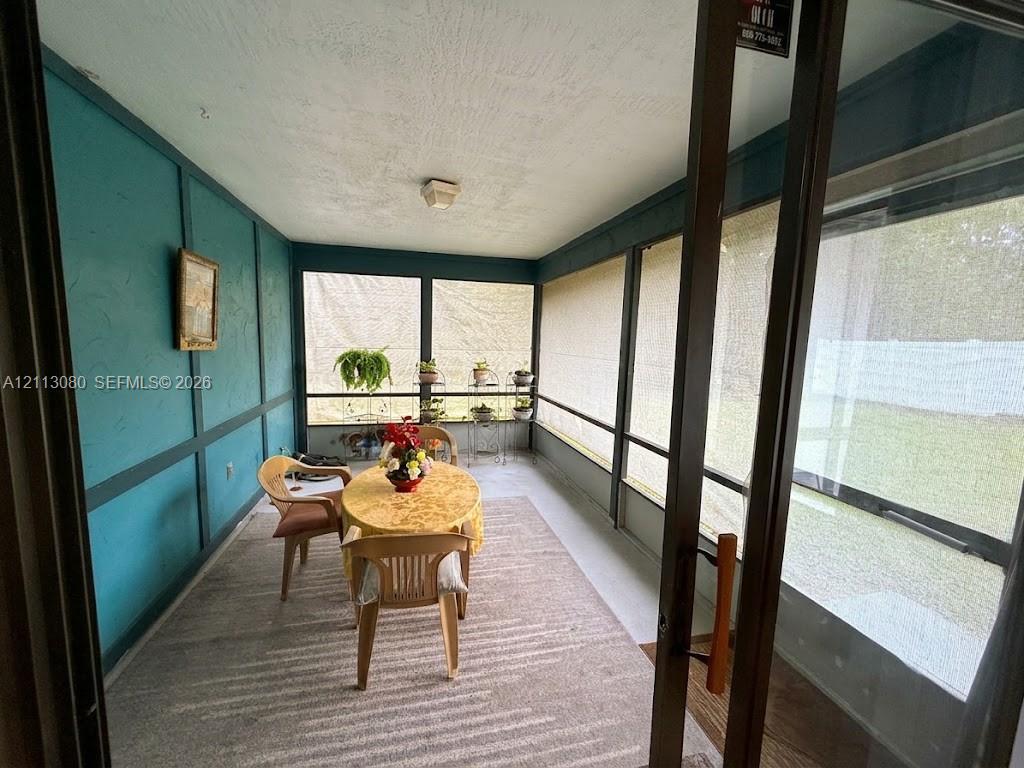 Enclosed sunroom featuring screen-paneled walls, a textured ceiling, dark-tone wall molding, and solid-surface flooring