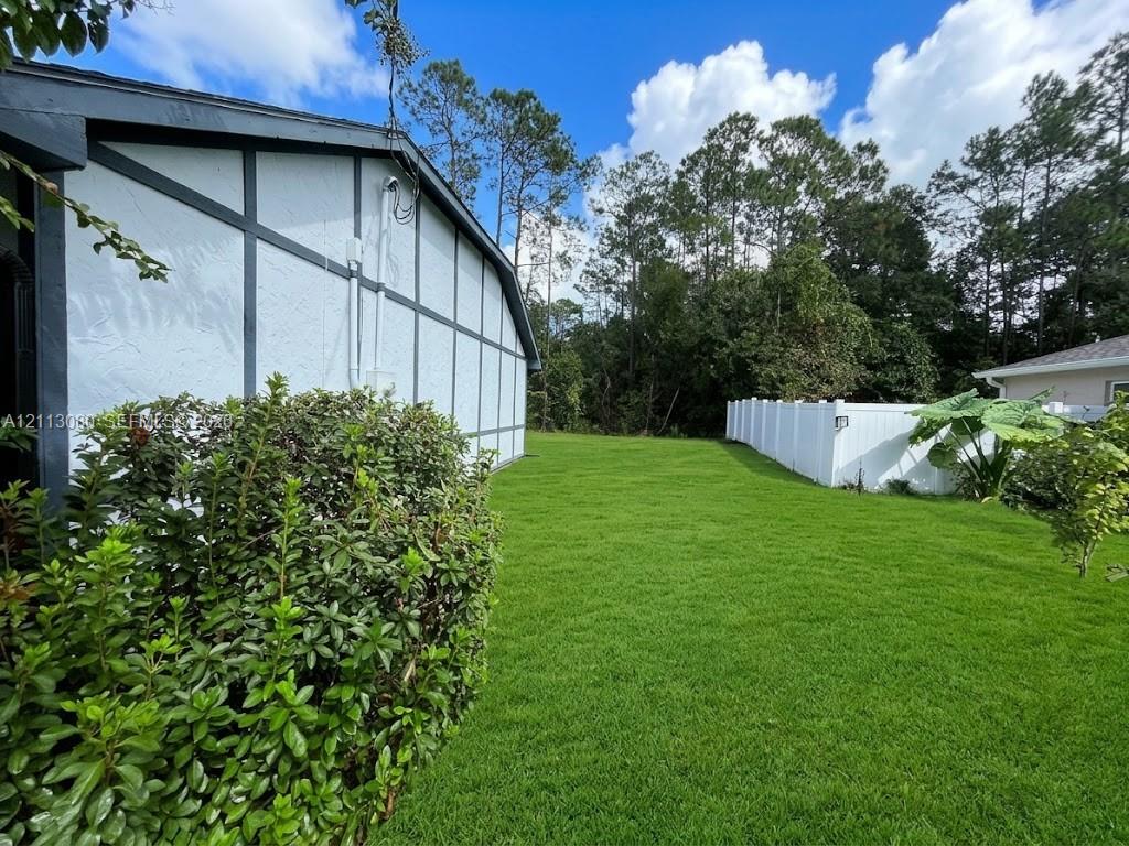 Side yard featuring a grass lawn, white vinyl fencing, and mature tree line