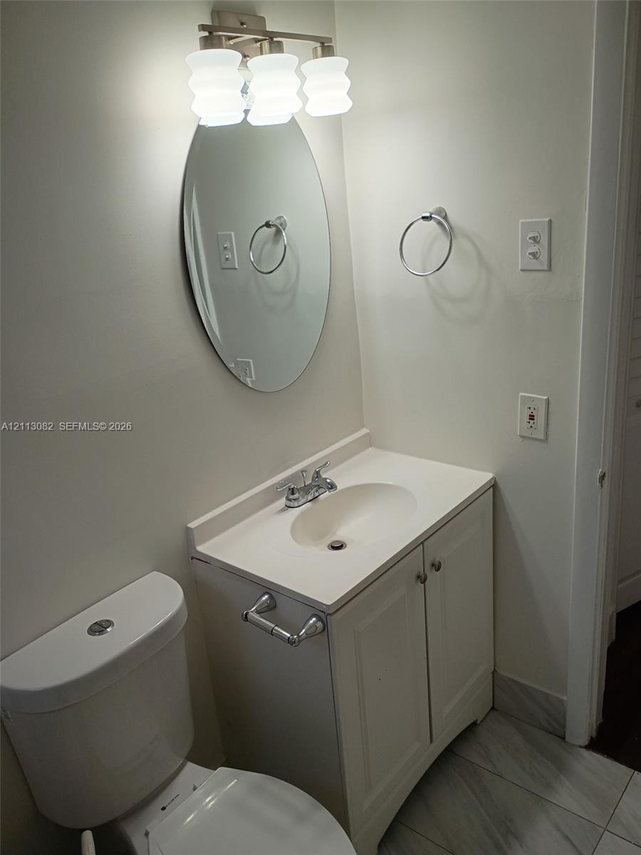 Bathroom featuring a white vanity cabinet with a integrated basin, oval wall-mounted mirror, three-light fixture, and stone-finish tile flooring