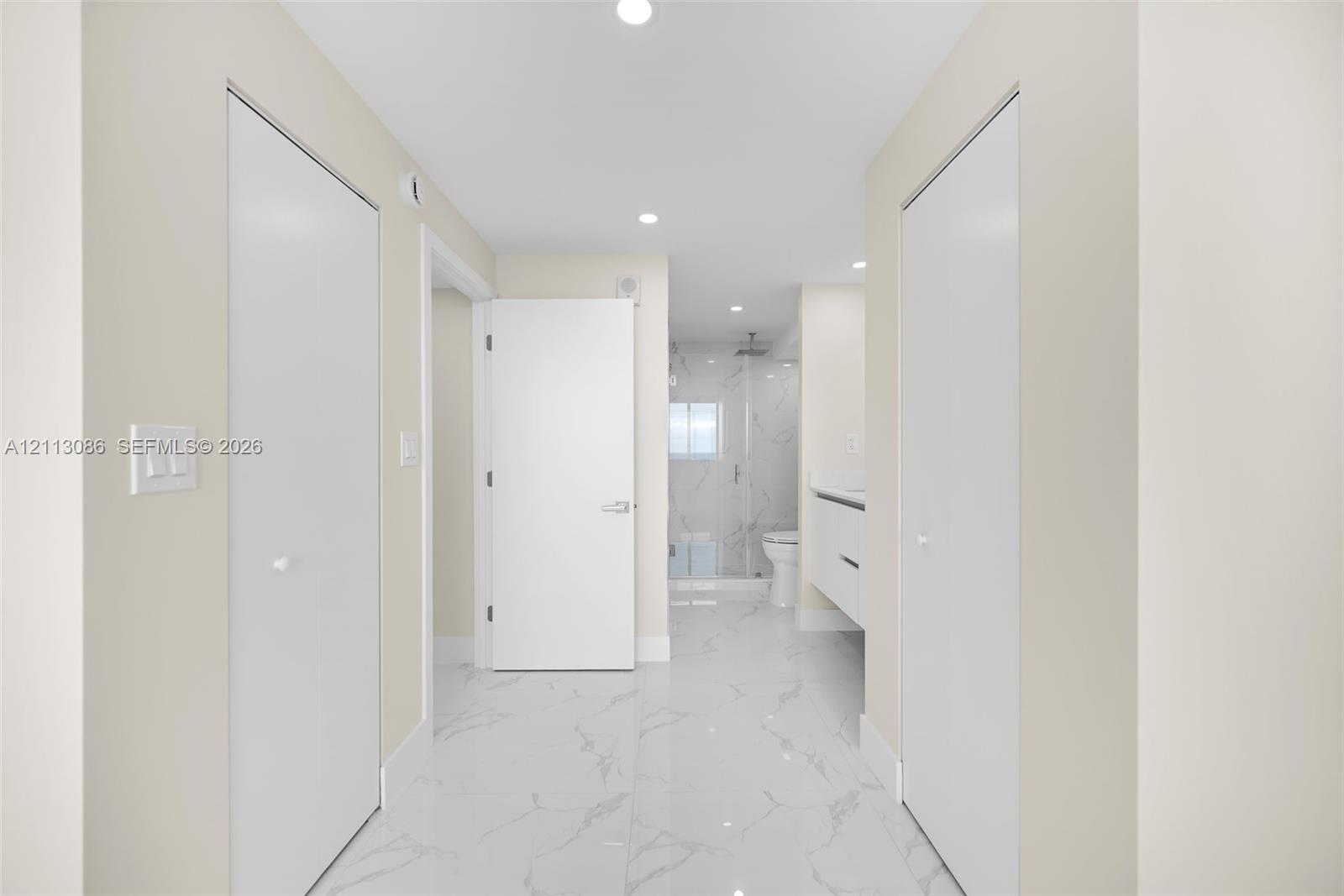 Hallway featuring high-gloss, large-format veined tile flooring, recessed ceiling lighting, dual floor-to-ceiling closets with white doors, and a modern wall-mounted floating vanity