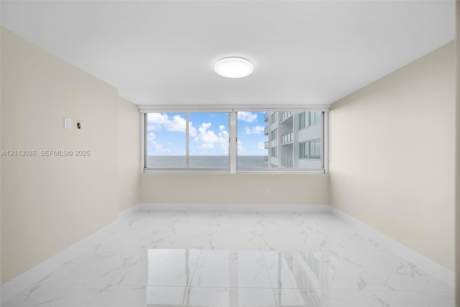 Spacious interior featuring white tile flooring with grey veining, neutral wall tones, large-format sliding windows, and flush-mount ceiling lighting