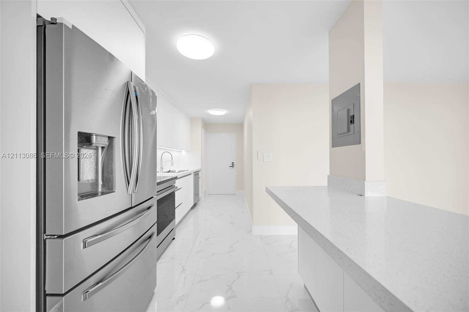 Kitchen featuring stainless steel refrigerator, white cabinetry, solid-surface countertops, and stone-finish tile flooring