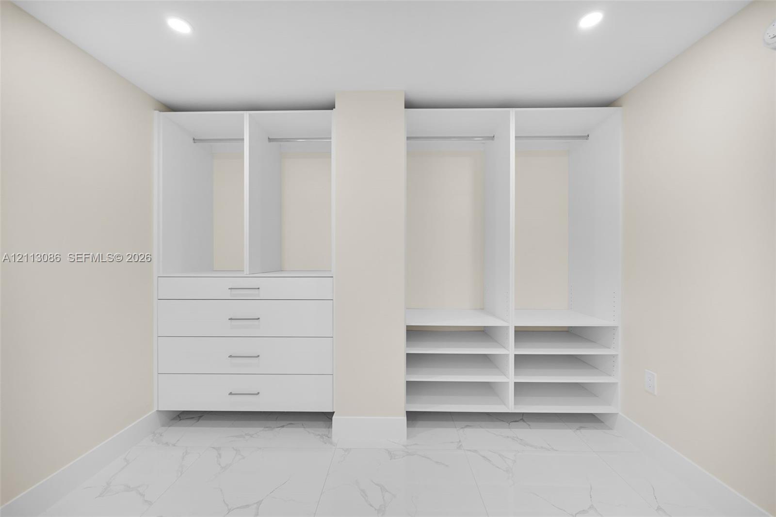 Custom white built-in cabinetry featuring hanging rods, four integrated storage drawers, and multiple open shelving units set against large-format, light-toned stone-finish flooring with prominent veining