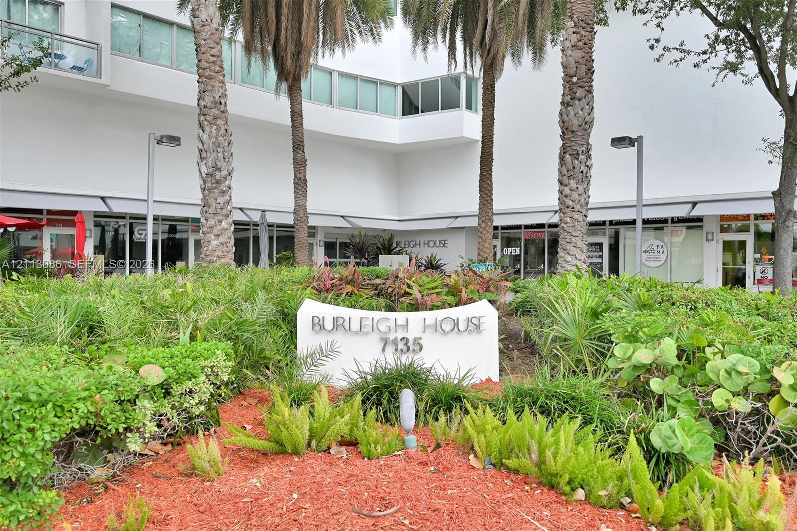 Exterior grounds featuring mature palm trees, tiered tropical landscaping, integrated signage, and architectural masonry