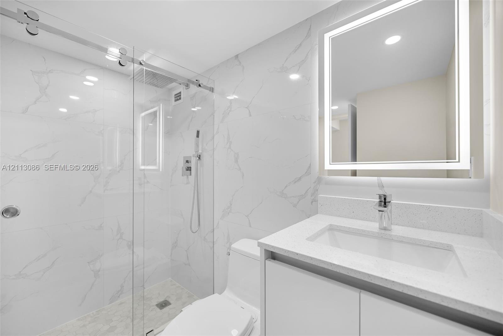 Bathroom featuring a glass-enclosed walk-in shower with stone-finish wall tile, a stone-composite countertop, a vessel-style sink, and a wall-mounted LED mirror