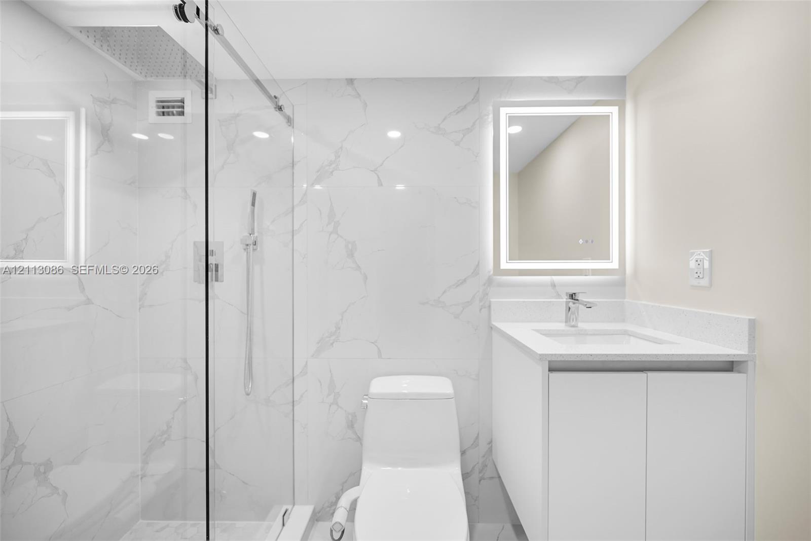 Walk-in shower with floor-to-ceiling large-format tile, frameless glass enclosure, wall-mounted vanity with integrated sink, and illuminated mirror