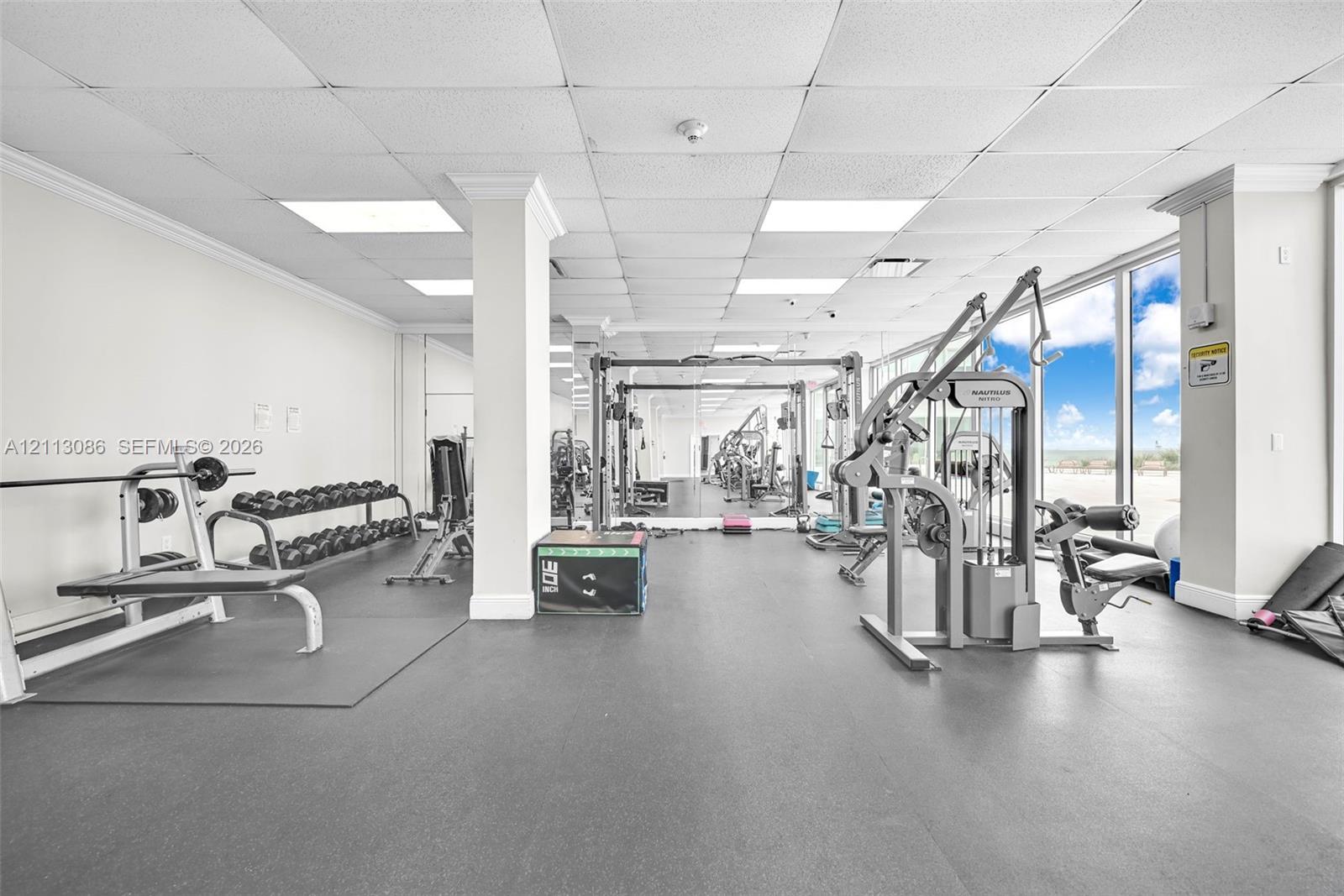 Fitness center featuring rubber flooring, ceiling-mounted recessed lighting, and wall-to-wall mirrored surfaces with floor-to-ceiling glass windows
