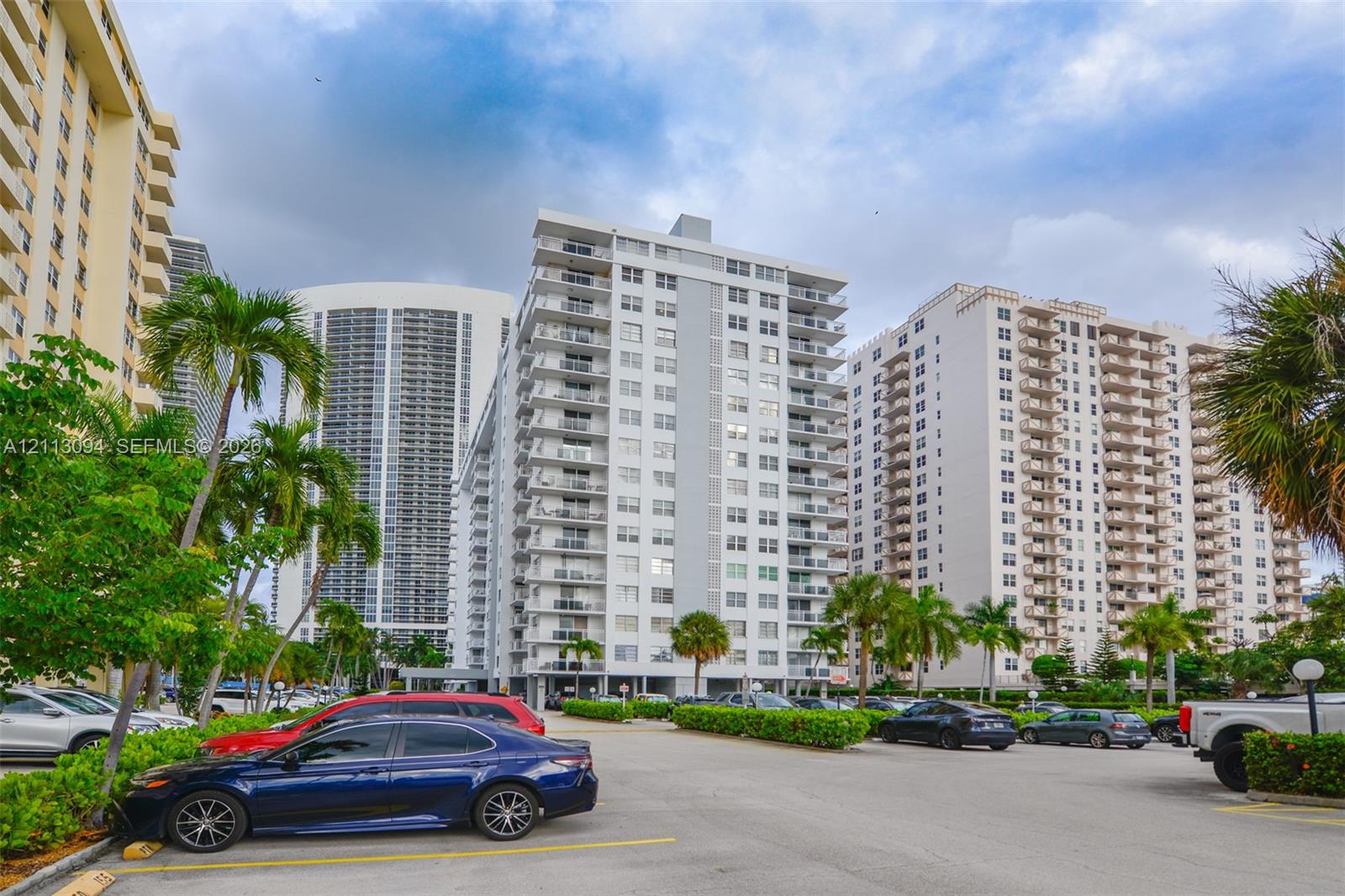 High-rise residential exterior featuring stacked private balconies, concrete construction, and landscaped grounds with mature palm trees
