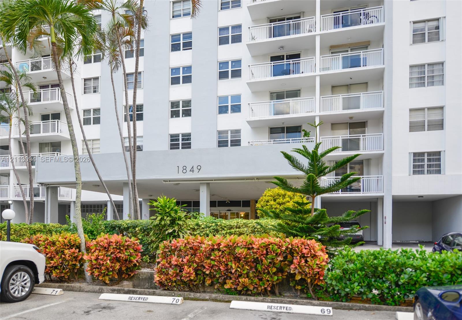 Multi-story residential exterior featuring private balconies with railings, a covered entrance canopy, and established exterior landscaping