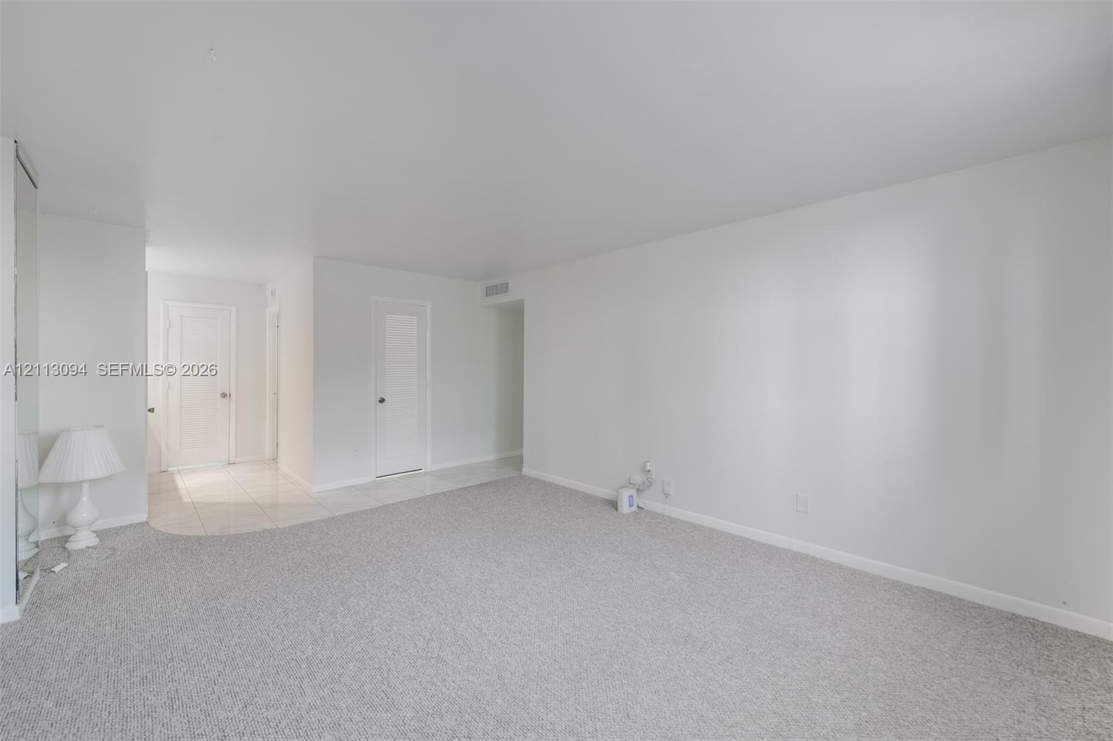 Neutral interior featuring plush wall-to-wall carpeting, light-colored tile flooring, solid-core interior doors, and floor-to-ceiling mirrored closet doors