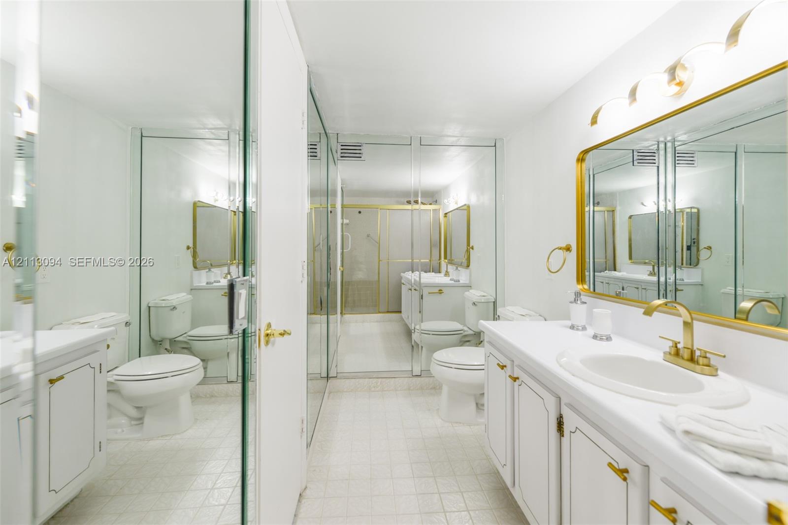 Bathroom featuring a white vanity with gold-tone hardware, an oval undermount sink, a framed gold-tone mirror, mirrored wall panels, and tiled flooring